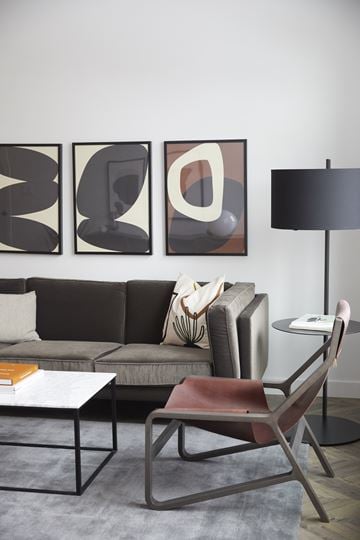 Calgary apartment for rent - A modern living room with a grey sofa, a coffee table, a chair, and three abstract paintings on the wall.