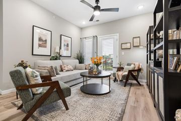 Louisville apartment for rent - A living room with a grey sofa, a round coffee table, a wooden chair, and a ceiling fan.