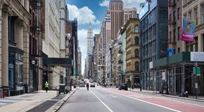 Queens apartment for rent - A city street with buildings on both sides and a few pedestrians walking.