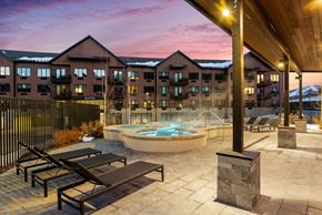 Park City apartment for rent - A pool area with sun loungers and a hot tub in front of a building with a mountain in the background.