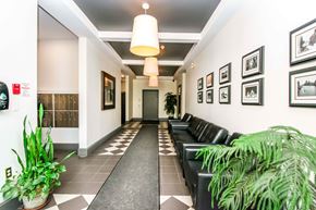 Halifax apartment for rent - A hallway with a black and white checkered floor and a row of black leather chairs on the right side.