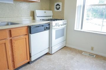 St. Louis apartment for rent - A white stove and dishwasher in a kitchen with wooden cabinets.