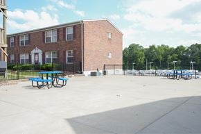 St. Louis apartment for rent - A red brick building with a white door and windows, a black fence, and a blue picnic table.