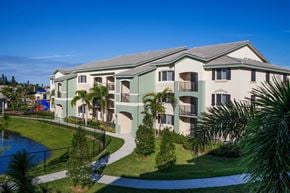 Pompano Beach apartment for rent - A building with a green roof and white walls with balconies and a pool in front.