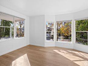 Santa Cruz townhouse for rent - A sunny room with a wooden floor and three windows showing trees and a street at Westmont Place Townhomes Apartments, Santa Cruz, CA, 95060