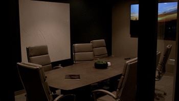 A conference room with a table, chairs, and a screen displaying the time.