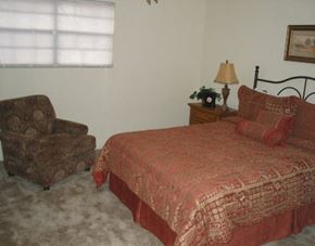 Tuscaloosa townhouse for rent - A bed with a red comforter and pillows sits in a room with a chair and a lamp.