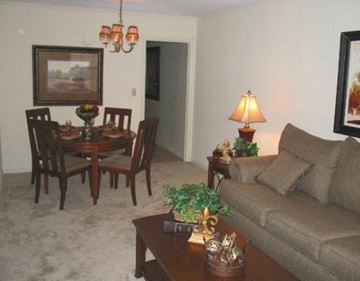 Tuscaloosa townhouse for rent - A living room with a brown couch, a dining table with chairs, a lamp, and a painting on the wall.