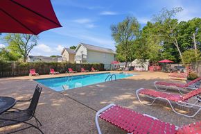 Tuscaloosa apartment for rent - A pool area with red lounge chairs and umbrellas.