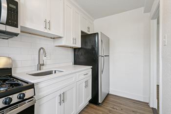 A black refrigerator is in a kitchen with white cabinets.
