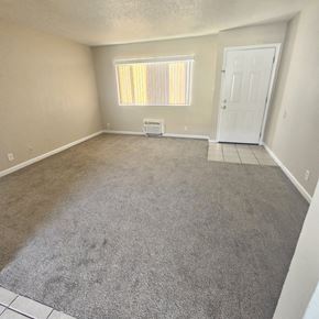 Antioch apartment for rent - A room with a carpeted floor, a window with blinds, a white door, and a small white table.