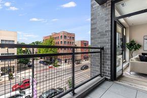 Chicago apartment for rent - A balcony with a black railing overlooks a parking lot and buildings.