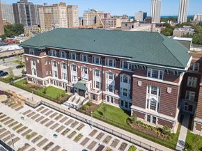 Chicago apartment for rent - A large red brick building with a green roof and a parking lot in front.