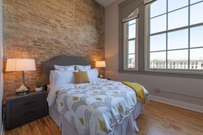 Chicago apartment for rent - A bedroom with a brick wall and a large bed with a white and yellow comforter.