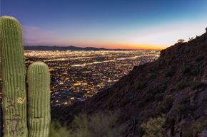 Phoenix apartment for rent - a view of the city at night from a hill with a cactus