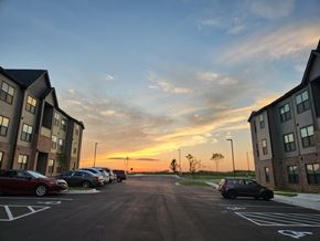 Claremore apartment for rent - A parking lot with cars parked and buildings on either side during sunset.