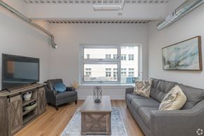 Lancaster apartment for rent - A living room with a grey couch, a wooden cabinet, a chair, and a coffee table.