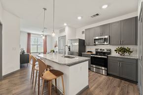 Cedar Hill apartment for rent - A modern kitchen with wooden chairs and stainless steel appliances at The Preserve at Preston Trails Apartments, Cedar Hill