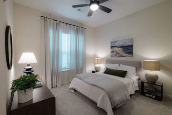 A bedroom with a large bed, a ceiling fan, and a painting on the wall