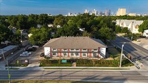 Dallas apartment for rent - A building with a red roof is surrounded by trees and a parking lot.