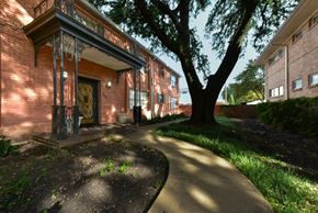 Dallas apartment for rent - A tree is in front of a building with a brick facade.