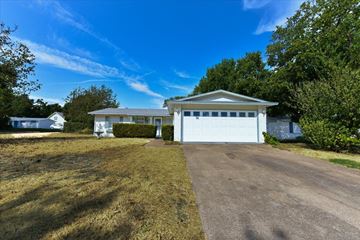 Dallas apartment for rent - A white house with a garage is surrounded by trees and grass.