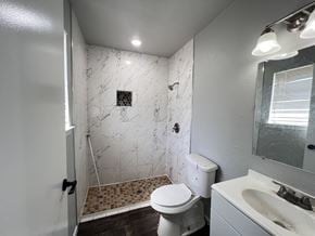 Dallas apartment for rent - A white toilet sits in a bathroom with a marble shower.