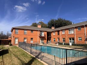 Dallas apartment for rent - A red brick apartment building with a pool in front.