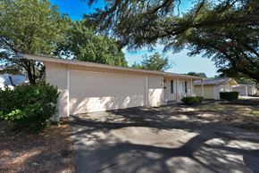 Richardson apartment for rent - A white building with a garage door is surrounded by trees.