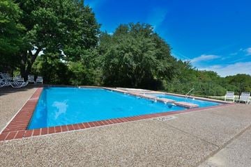 Dallas apartment for rent - A large outdoor swimming pool surrounded by trees and lounge chairs.