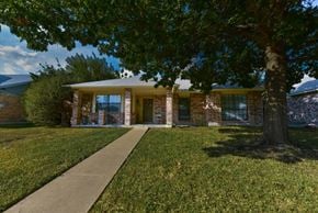 Garland apartment for rent - A house with a brown brick exterior and a large tree in front.