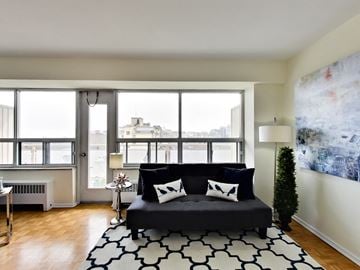 Toronto apartment for rent - A black couch with white pillows sits in a living room with a large window.