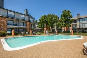 Dallas apartment for rent - A swimming pool surrounded by a fence and chairs in front of a building.