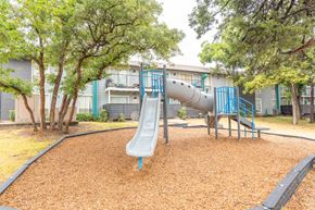 Dallas apartment for rent - a playground with a slide and trees in front of a building