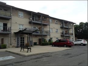 Kingston apartment for rent - an apartment building with a bench and cars parked in front