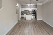 Dallas townhouse for rent - Open living room and kitchen with wood-look flooring, breakfast bar, and pendant lighting in a one-bedroom apartment at The Brownstones in Far North Dallas