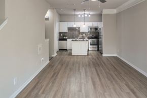 Dallas townhouse for rent - Open living room and kitchen with wood-look flooring, breakfast bar, and pendant lighting in a one-bedroom apartment at The Brownstones in Far North Dallas