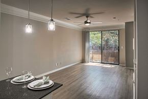 Dallas townhouse for rent - Open-concept living and dining area with wood-look flooring, ceiling fan, and sliding glass door in a one-bedroom apartment home
