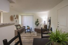 Dallas apartment for rent - View of the living room with a couch, chaise lounge and a potted plant from the dining room of a 515 square foot 1 bedroom, 1 bath apartment home at Canyon Creek Apartments in Dallas Midtown neighborhood of Dallas, TX.