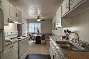Fairfield apartment for rent - Galley kitchen in the Fairfield Pointe 850 sq. ft. 1-bedroom apartment, with white cabinets, sink, range, refrigerator, and dining area beyond.