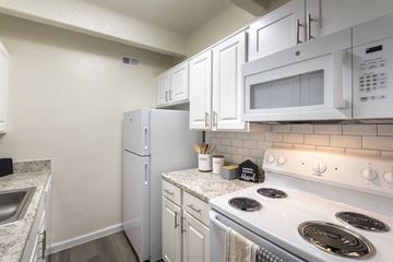 Dallas apartment for rent - A kitchen with a white stove top oven, white microwave, and white cabinets.
