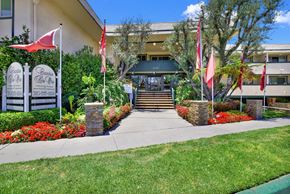 Torrance apartment for rent - the front of a building with flags and a sidewalk at Camino de Oro Apartments, Torrance, CA