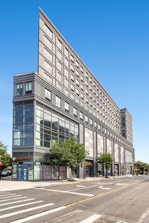 Bronx apartment for rent - A large grey building with a blue sign on the ground floor.