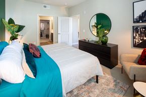 Los Angeles apartment for rent - Apartments in South Gate, CA, with In-Unit Washer and Dryer - SoLa - A Cozy Bedroom With A White Bed And Teal Bedding, Black Dresser With Round Mirror, And An Accent Chair.