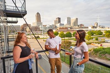 Three people are standing on a balcony with a city skyline in the background.
