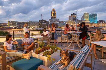 A group of people are sitting on a rooftop terrace with a city skyline in the background.
