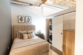 Newton apartment for rent - A bedroom with a bed, pillows, and a washing machine in the laundry area.at Plant 1 Lofts, N. Newton, 50208  