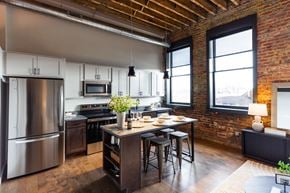 Newton apartment for rent - A kitchen with a large stainless steel refrigerator and a wooden table with chairs.at Plant 1 Lofts, N. Newton, IA 50208  