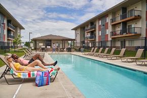 Grimes apartment for rent - A woman in a yellow bikini lounges by a pool with a man in a pink shirt at Meadowlark Place Apartments, Grimes, IA,  50111