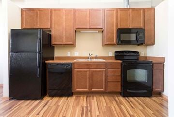 Des Moines apartment for rent - A black refrigerator, microwave, and oven in a kitchen with wooden cabinets.